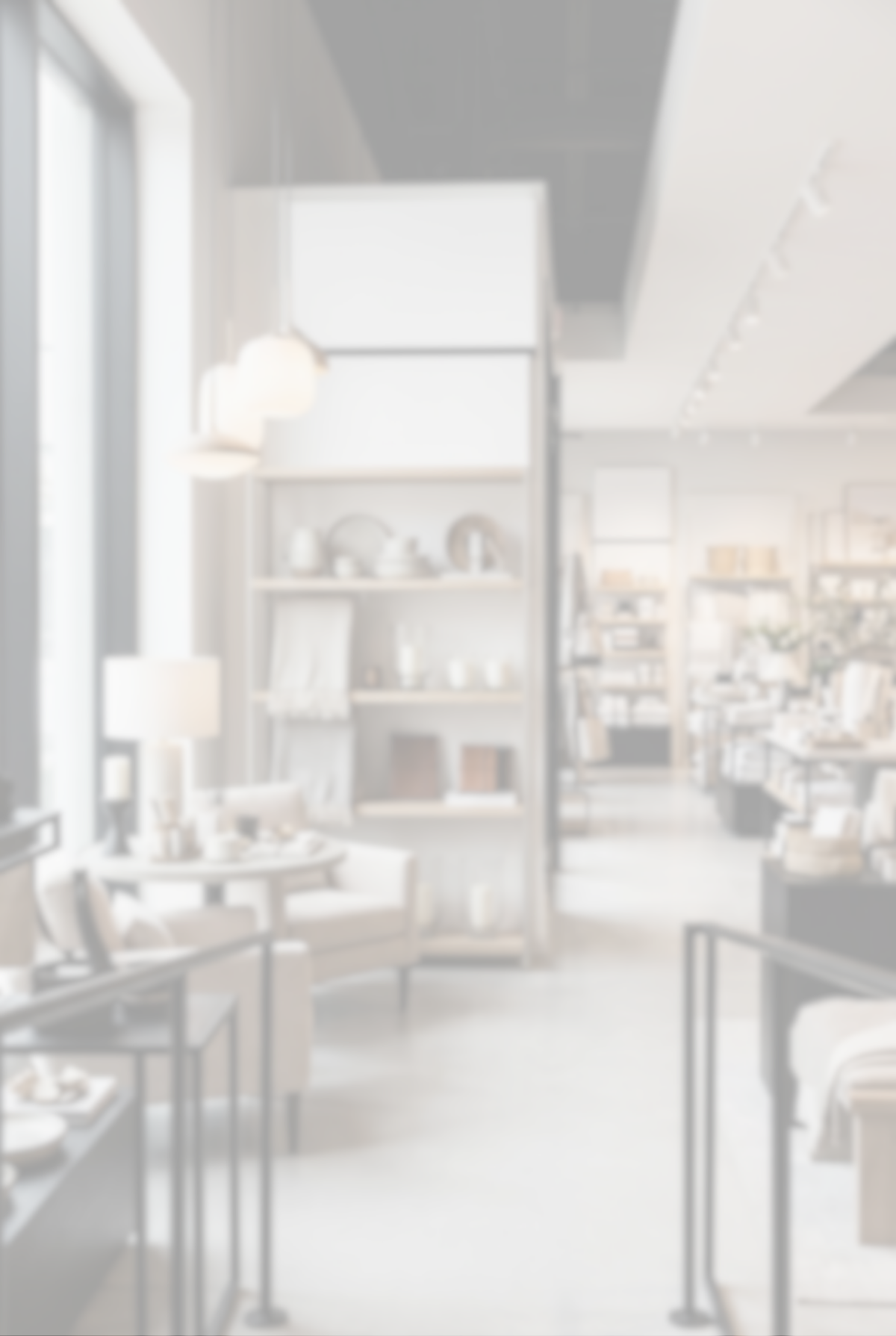 A bright, airy home decor showroom interior with white shelving, hanging pendant lights, chairs, tables, and display fixtures in a minimalist, high-key style.